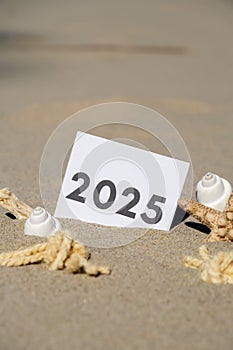 2025 text start new year symbol on paper greeting card on background of starfish summer vacation decor. Sandy beach sun