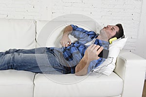 20s or 30s man having fun lying on couch listening to music on mobile phone with headphones playing air guitar