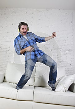 20s or 30s man jumped on couch listening to music on mobile phone with headphones playing air guitar