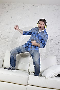 20s or 30s man jumped on couch listening to music on mobile phone with headphones playing air guitar