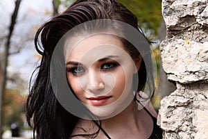 20s caucasian brunette leans forward next to stone wall