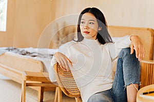 20s young teenage Asian woman wears a sweater looking away in stylish cozy room background. Attractive female model