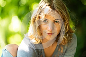22 yo blonde woman, close up with a natural green bokeh background