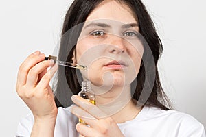 A 25-30 year old brunette woman applies anti-wrinkle serum or oil to her face. Facial skin care, acid peeling