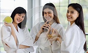 3 Asian women with long black hair in white robes, standing and holding wood plate spa massage equipment, herbal compress ball,