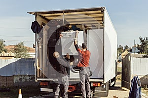 3 colleagues of a moving company load a dishwasher onto the truck