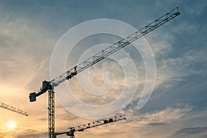 3 cranes at construction site against sunset sky