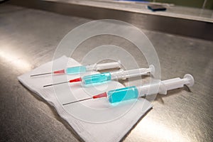 3 differently sized syringes filled with blue liquid lie on a white compress