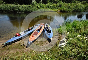3 kayaks on the bank of a small river in summer