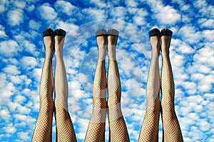 3 pairs of sexy female legs in black fishnets against a cloudy background