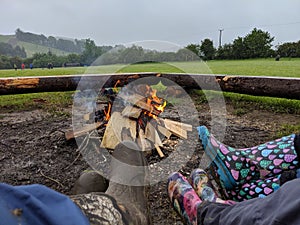 3 people in pairs of Wellington boots sitting around a campfire