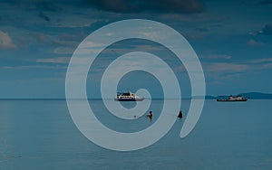 3 people standing in calm water fishing with boats in the back ground