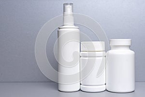 3 plastic containers for medicines and vitamins, a bottle with a spray bottle on a gray background