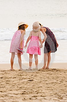 3 sisters stand on beachfront facing the ocean.Whispering in sis