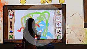 A 3 year old girl plays with an application to draw and color on the wall through the use of a projector