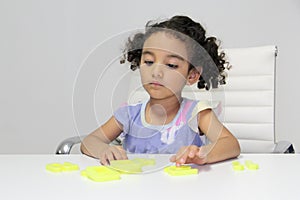 3-year-old Latina girl with brunette and curly hair plays with a game of letters and numbers for learning within the autism