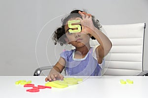 3-year-old Latina girl with brunette and curly hair plays with a game of letters and numbers for learning within the autism