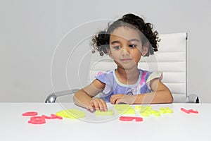 3-year-old Latina girl with brunette and curly hair plays with a game of letters and numbers for learning within the autism