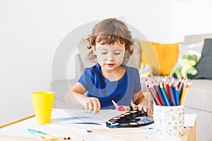 3 years girl painting at the small table at home.