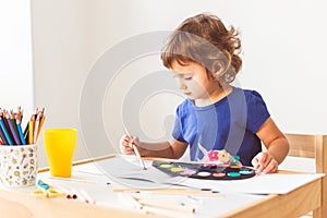 3 years girl painting at the small table at home.