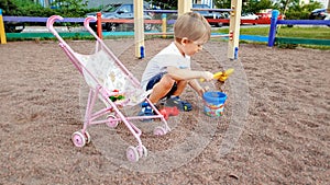 3 years old toddler boy playing with pram for dolls on the playground