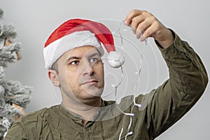 A 30-35-year-old man in a red hat takes out a Christmas tree garland from a wooden basket.