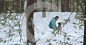 A 30 year old man and his dog are having fun and playing in the winter forest