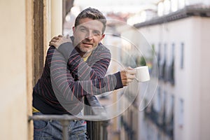 30s or 40s attractive and happy man at home balcony relaxed and cheerful enjoying cup of coffee looking to city street smiling and