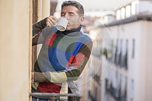 30s or 40s attractive and happy man at home balcony relaxed and cheerful enjoying cup of coffee looking to city street smiling and