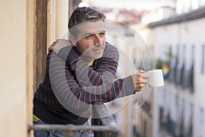 30s or 40s attractive and happy man at home balcony relaxed and cheerful enjoying cup of coffee looking to city street smiling and