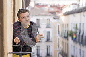 30s or 40s attractive and happy man at home balcony relaxed and cheerful enjoying cup of coffee looking to city street smiling and