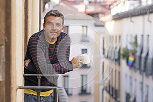 30s or 40s attractive and happy man at home balcony relaxed and cheerful enjoying cup of coffee looking to city street smiling and
