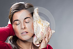 30s brunette woman listening to the ocean sound from a giant shell