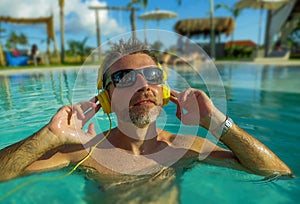 30s cool and relaxed man enjoying playful at tropical luxury resort swimming pool listening to music with headphones feeling