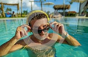 30s cool and relaxed man enjoying playful at tropical luxury resort swimming pool listening to music with headphones feeling