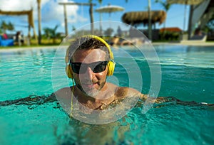 30s cool and relaxed man enjoying playful at tropical luxury resort swimming pool listening to music with headphones feeling