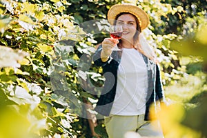 30s Woman in hat tasting red wine in vineyard. Portrait of pretty young woman holding glass of wine. Happy vintner