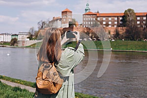 30s woman tourist in stylish clothes making photo at camera the famous Wawel Castle in Krakow. Attractive young female