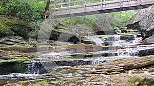 31 second video mini waterfall with mossy rocks under walking bridge
