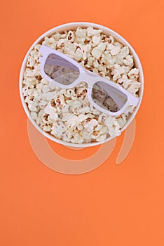 3d glasses lie on a cup with popcorn isolated on a orange background. Cinema Concept