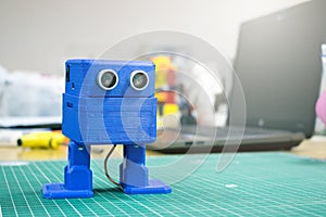 3D printed Funny dancing blue robot on the background of devices and laptop. Robot model printed on automatic three dimensional 3d