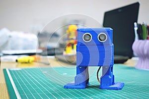 3D printed Funny dancing blue robot on the background of devices and laptop. Robot model printed on automatic three dimensional 3d
