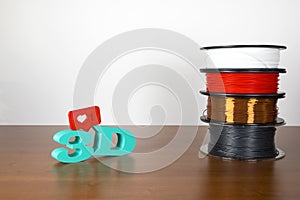 3D printing filament reels with text `3d` and a simbol of heart on wooden background