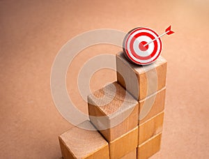 3d red target dart icon on top of wooden blocks graph steps on brown kraft paper background. Business target, growth process,