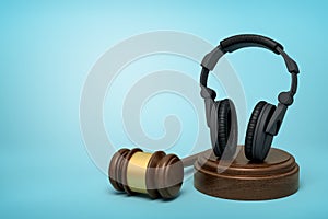 3d rendering of black headphones standing upright on sounding block with judge gavel beside on light-blue background.