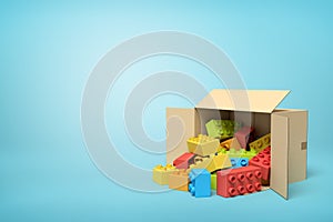 3d rendering of cardboard box lying sidelong full of colorful toy bricks on blue background.