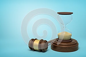 3d rendering of hourglass standing on sounding block with gavel lying beside on light-blue background with copy space.