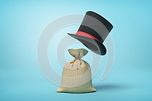 3d rendering of light-brown canvas money sack and big black tophat floating in air above it on light blue background.