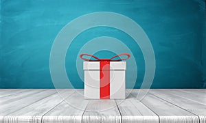 3d rendering of a lone white gift box with a red bow standing on a wooden desk in front of a blue background.