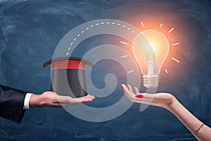 3d rendering of a male businessman`s hand holding a wizards hat and a female hand holding a bright glowing lamp.